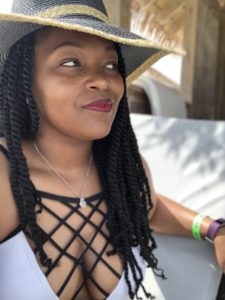 Black woman wearing a black and goal summer hat while smiling