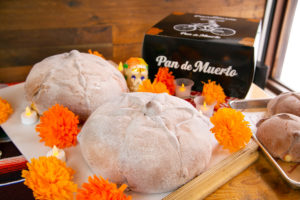 loaves of pan de muerto displayed with candles and orange marigolds and a bakery box