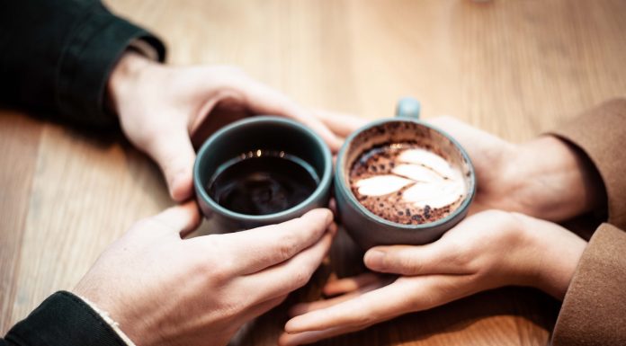 couple holding cups of coffee together on table