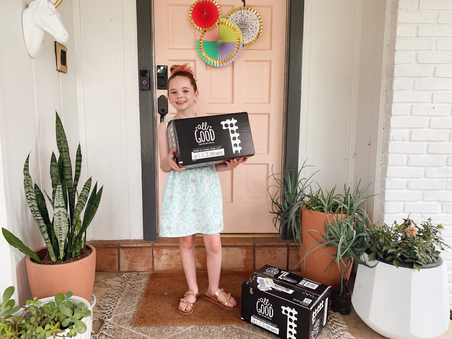 big sister holding box of All Good diapers in front of front door