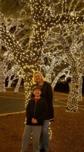 a mother and son under trees wrapped in white holiday lights