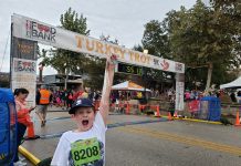 young boy holding a race medal in front of a finish line