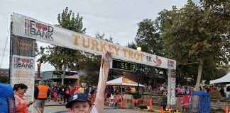 young boy holding a race medal in front of a finish line