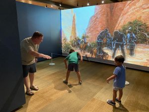 children and a man doing motions in front of an immersive exhibit