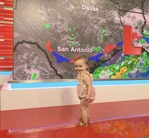 a toddler in a tv studio in front of a weather screen