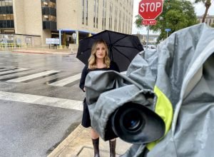 a reporter in the rain with an umbrella and camera