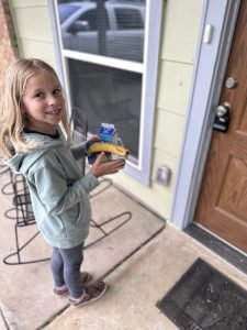 Family volunteer opportinutiy with Meals on Wheels San Antonio - a young girls waits at a front door with food that she is dropping off.