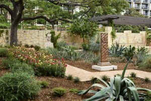 flowers and sculptures in a garden with a stone wall